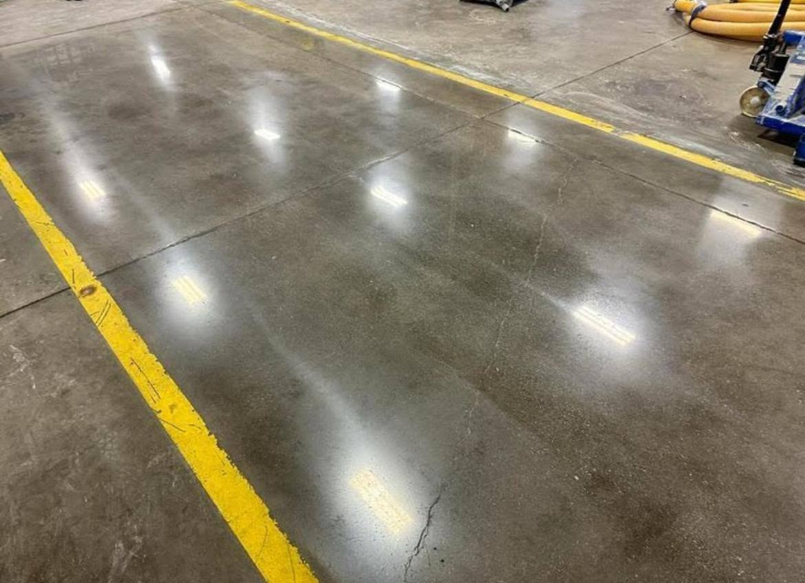 Piso de concreto pulido en nave industrial, con líneas de seguridad amarillas y reflejos de la iluminación